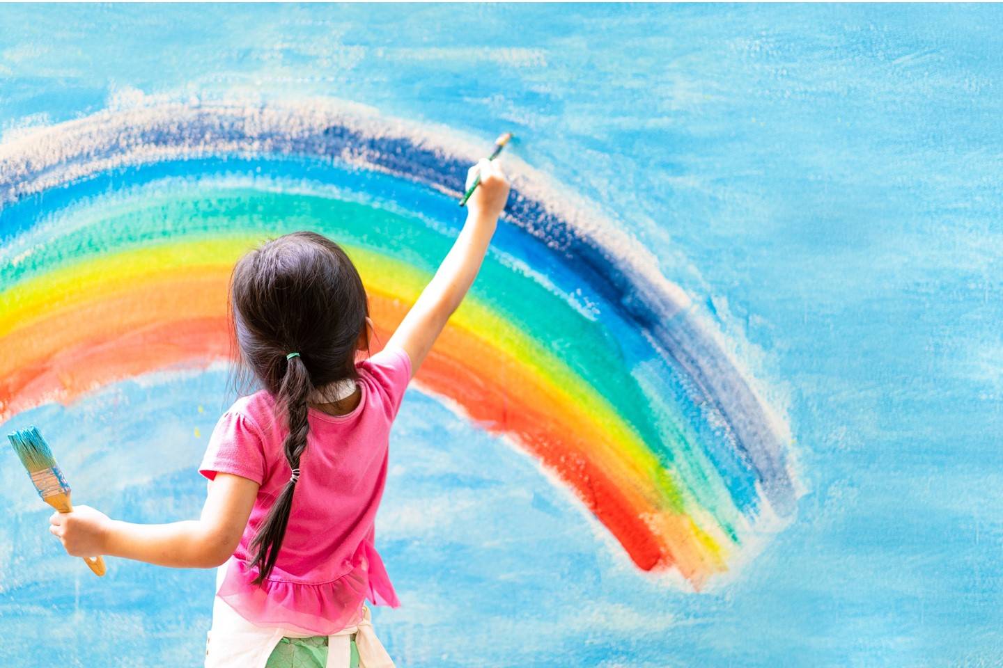 A girl paints a rainbow on a blue wall