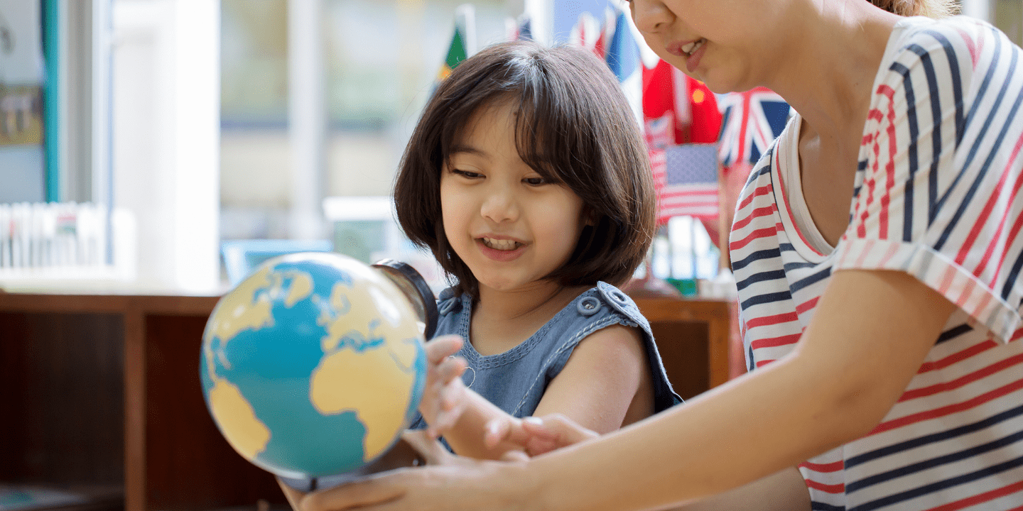 Student looks happily at world globe with teacher