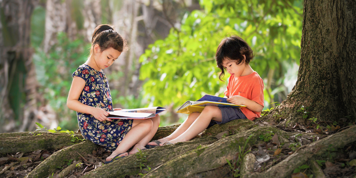 Girl and boy reading under the shade of a tree
