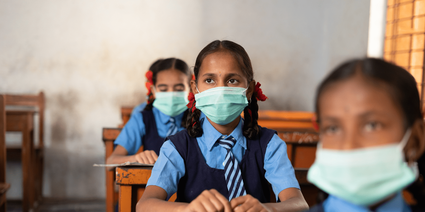 Girl in India sits in classroom with mask on