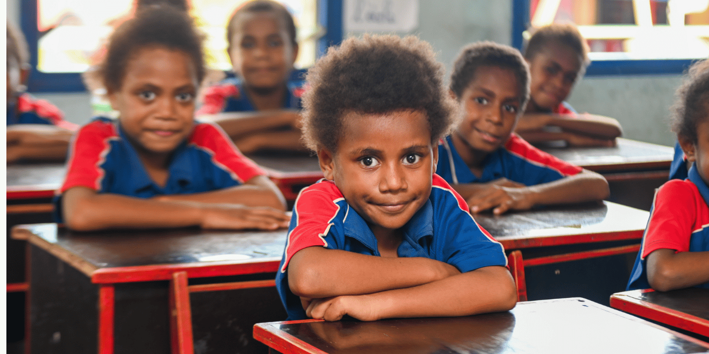 Vanuatu boy in classroom looks at camera.