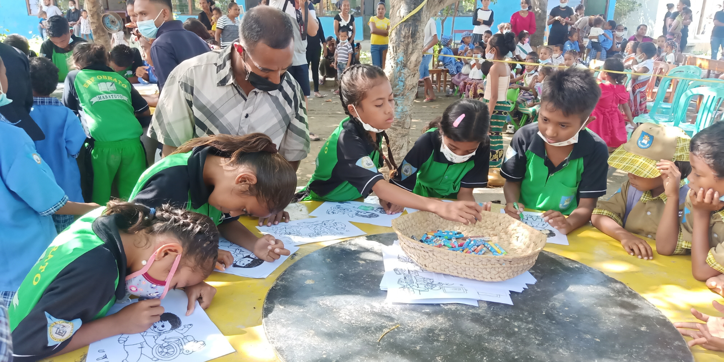 Students in Timor-Leste colour in drawings with supervision from teacher