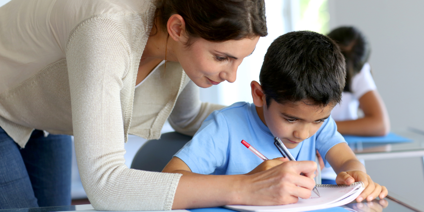 Stock image of a teacher helping young boy with a writing lesson.