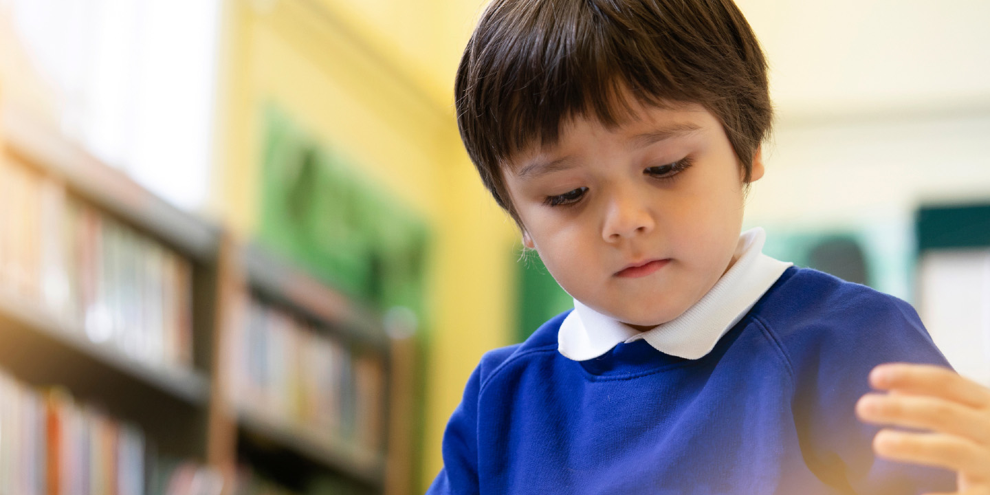 Preschool boy enjoy reading a book in the library with blurry background of bookshelf.