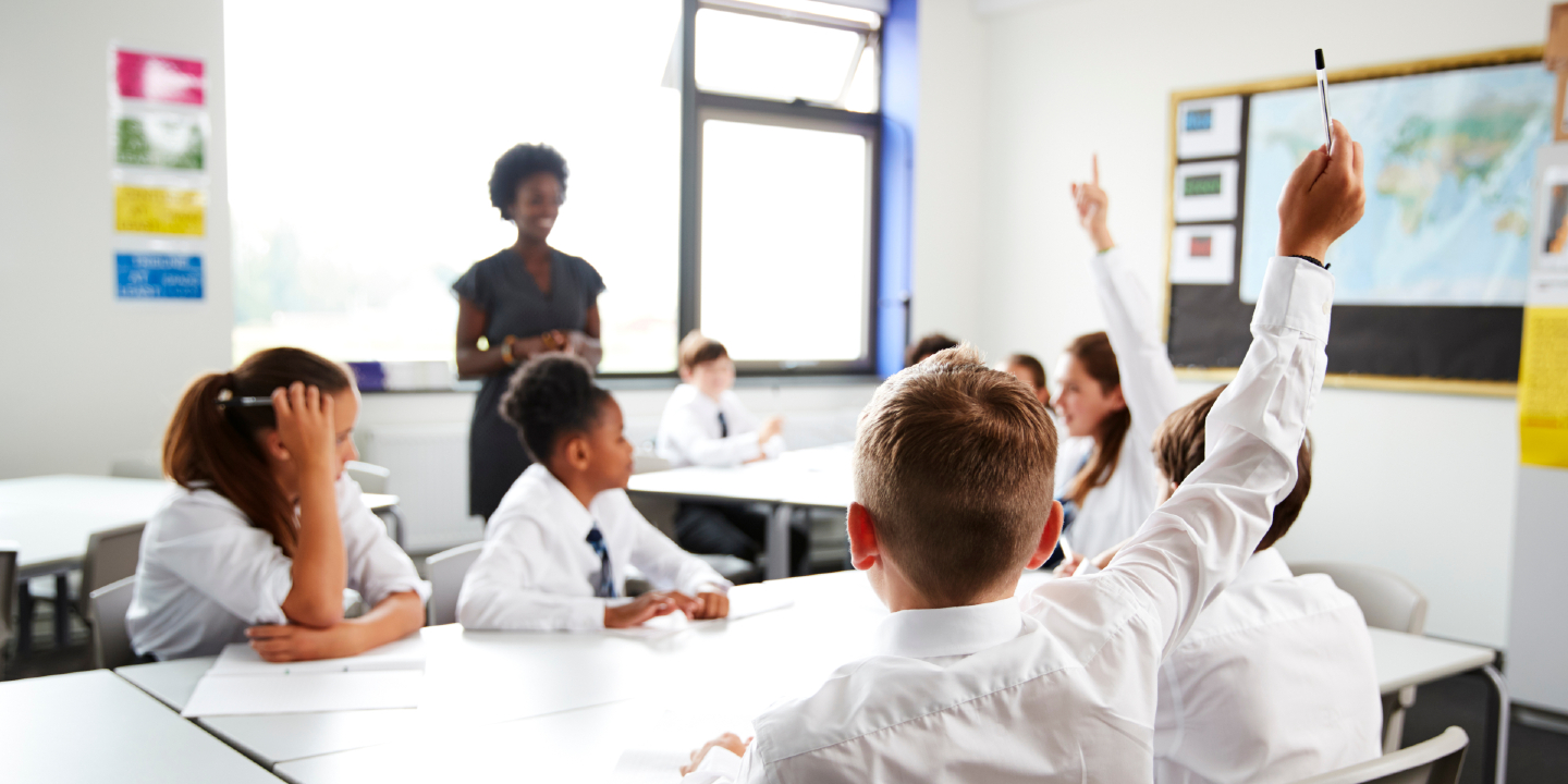 Stock image of high school students wearing uniform raising hands to answer question set by teacher In classroom.