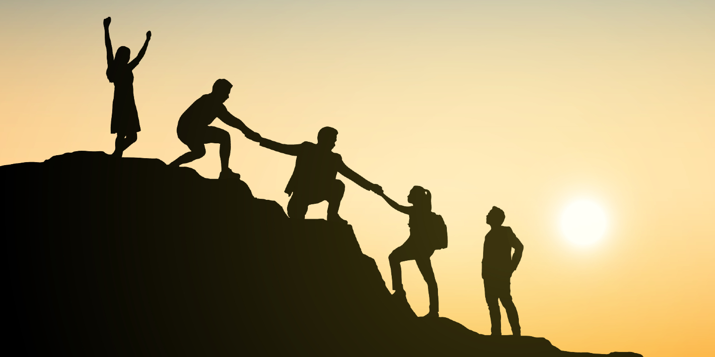 Stock image of silhouettes of group of business people climbing on mountain and helping each other at sunset.