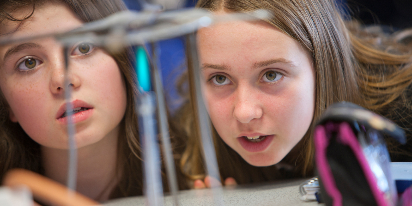 Stock image of female high school students using Bunsen burner in science class.