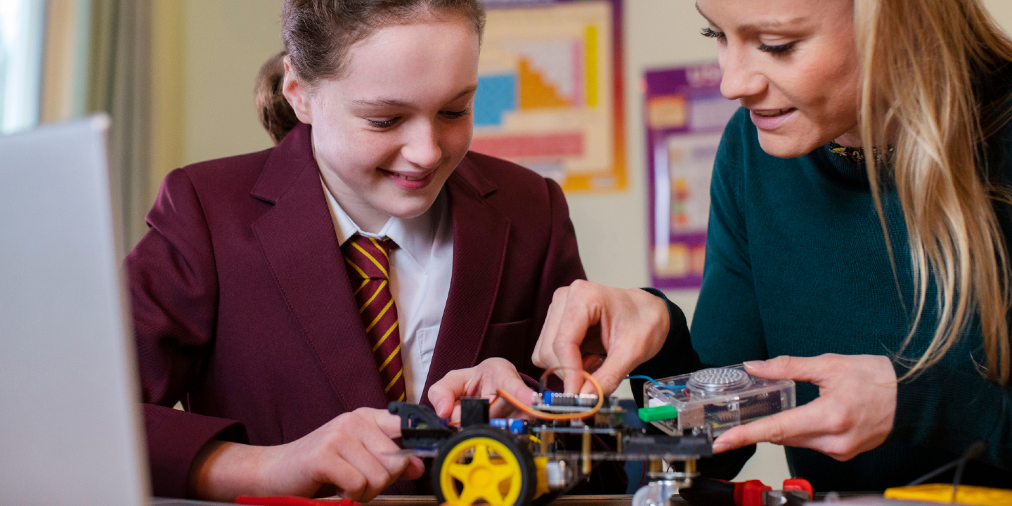 Stock image of a Teacher Helping Female Pupil Wearing Uniform To Build Robot Car In Science Lesson