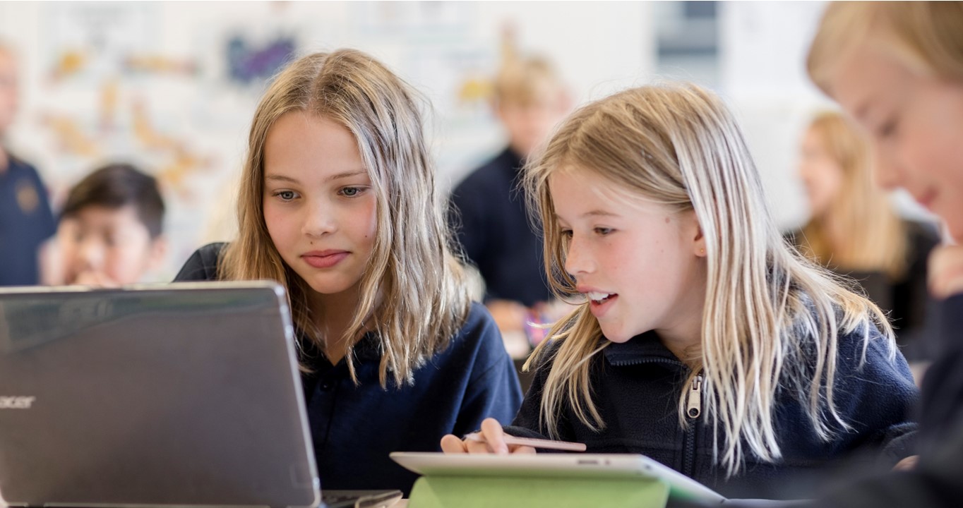 Stock image of two female school students looking at a laptop screen.