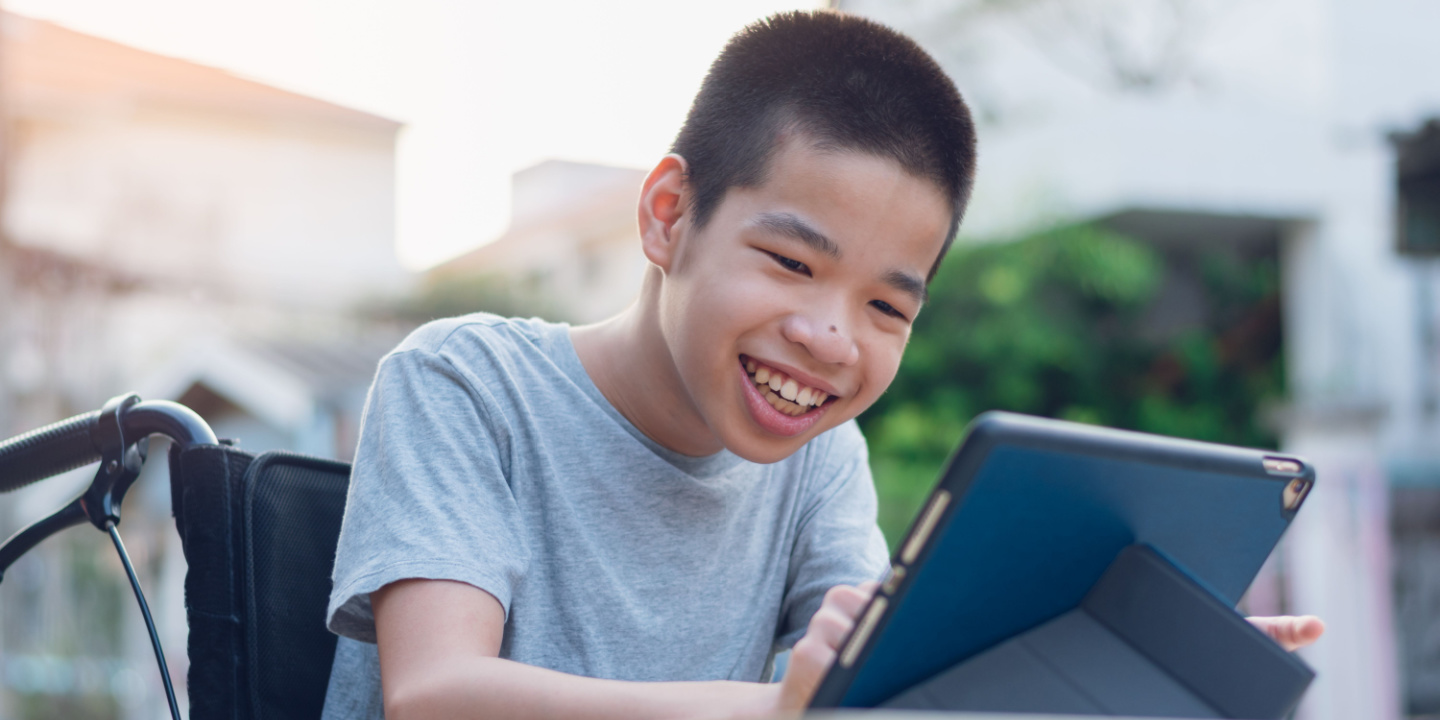 A young boy is sitting in his wheelchair looking at a laptop screen