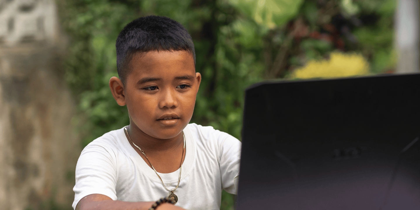 Stock image of a child in Southeast Asia looking at a laptop.
