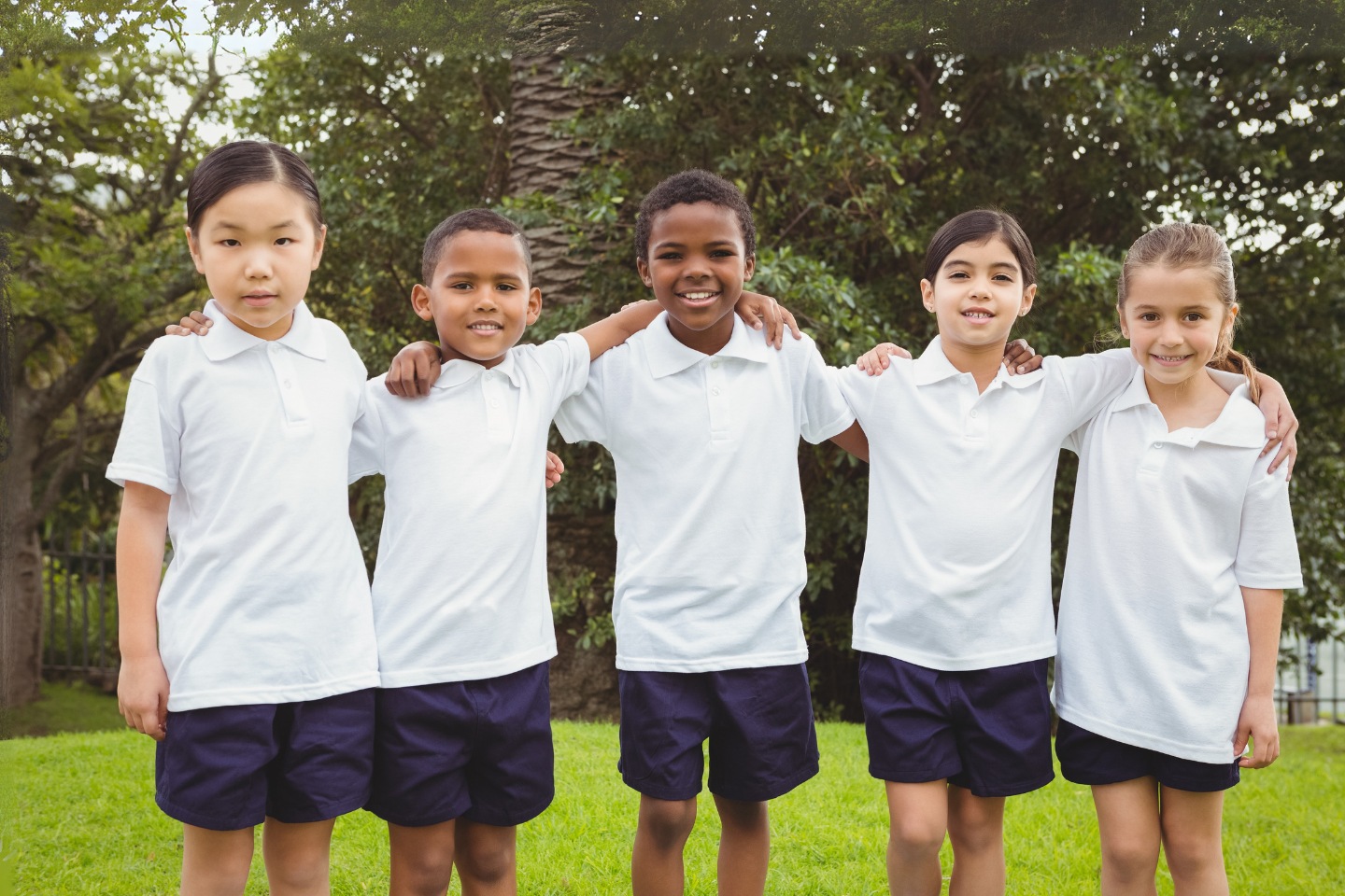 Five primary school aged children in white t-shirts stand with arms around each other. Four are smiling.